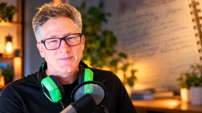 Dave Bailey sitting in a warmly lit recording studio, wearing green headphones with a microphone in front of him.